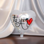 Globo plateado en forma de corazón con la frase te amo y un corazón rojo dibujado, sobre fondo de tela blanca difuminada