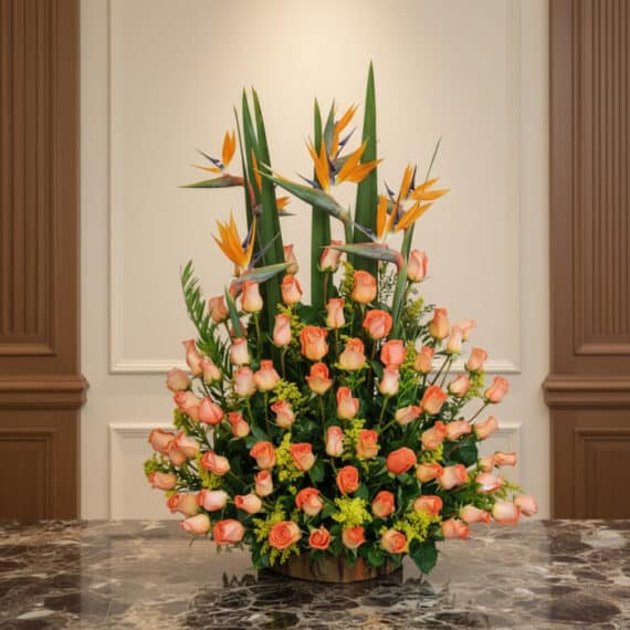 Arreglo floral grande con rosas color salmón y aves del paraíso, sobre una mesa de mármol en un entorno elegante de hotel bou
