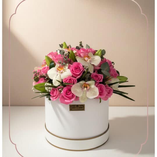 Arreglo floral TANIA con rosas rosadas vibrantes y orquídeas blancas delicadas en una caja redonda blanca con borde dorado, i