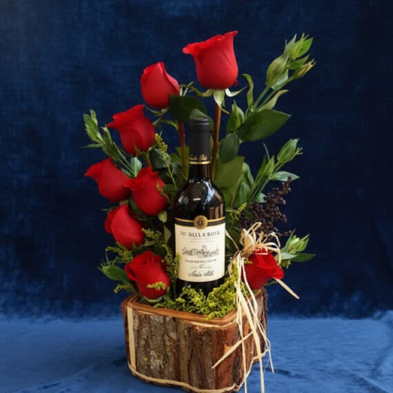 Arreglo Floral VERITA: Rosas Rojas y Vino para un Regalo Apasionado Arreglo floral VERITA con rosas rojas frescas y una botella de vino tinto, presentado en una base de madera rústica, ideal pa