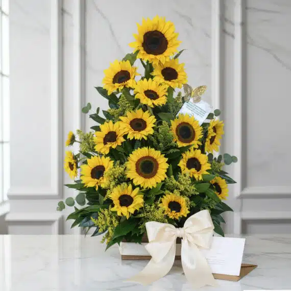 Impresionante arreglo floral con girasoles vibrantes, follaje verde y un lazo de satén, presentado sobre una mesa de mármol.