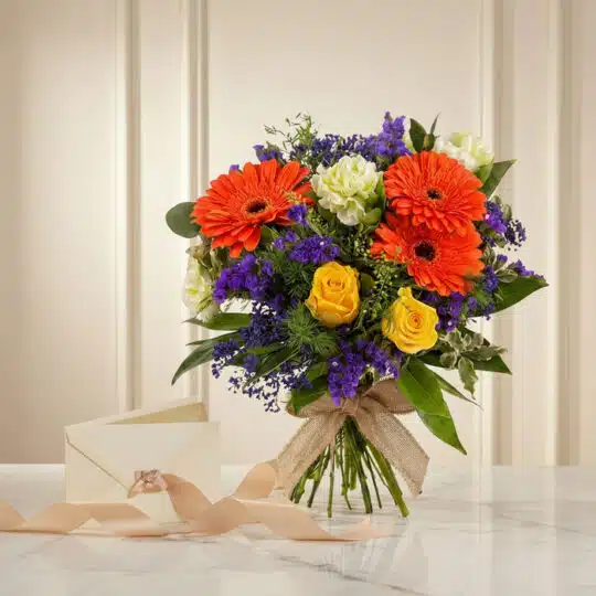Bouquet Floral SABRINA con rosas amarillas, gerberas naranjas, flores moradas y follaje verde, atado con cinta de yute, sobre