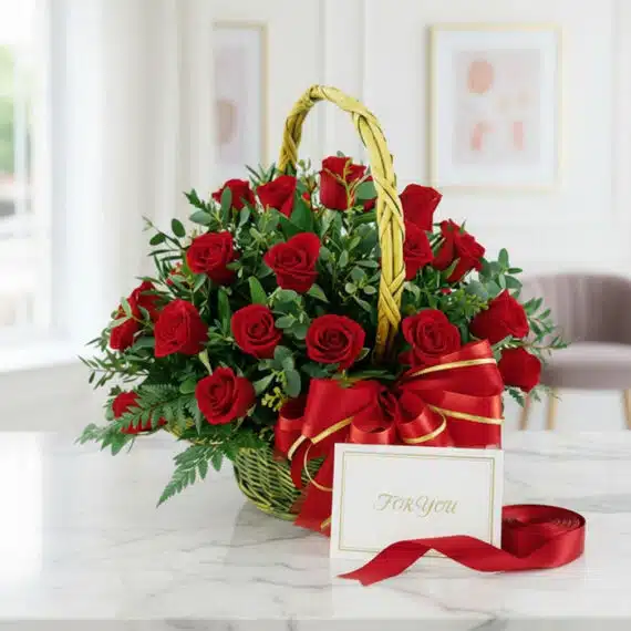 Canasta floral de lujo con 24 rosas rojas vibrantes, follaje verde, lazo de satén rojo y tarjeta de regalo 'For You' sobre má