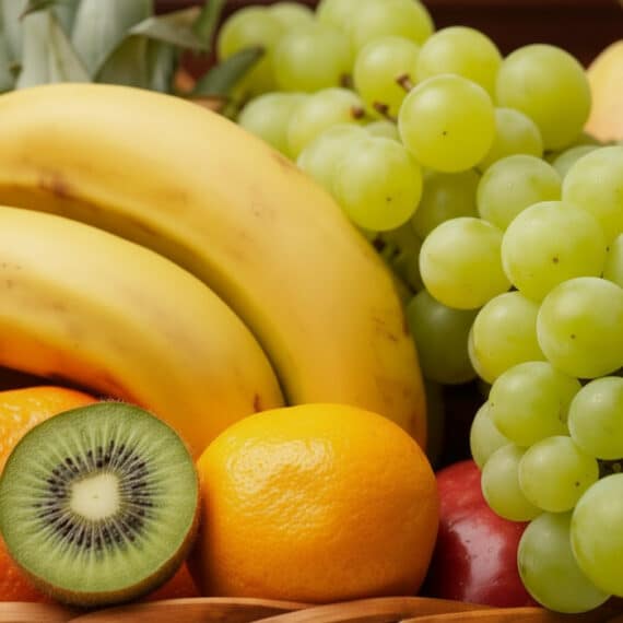 Primer plano de una canasta de frutas Corvus con plátanos, uvas verdes, kiwi, naranja y manzana, destacando su frescura y col
