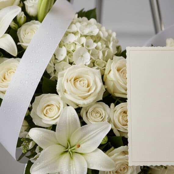 Fotografía macro premium de la Corona Refugio de Paz, con rosas blancas, lirios y hortensias, pétalos con rocío sutil y cinta