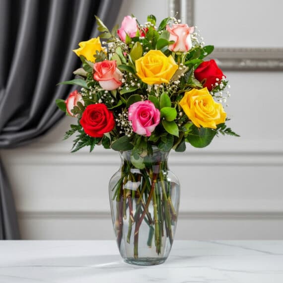 Jarrón con 12 Rosas Multicolor: Frescura y Elegancia para Regalar Jarrón de cristal transparente con un ramo de 12 rosas de colores variados: rojas, amarillas, rosas y blancas, con follaje ve
