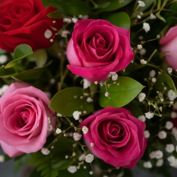 Primer plano extremo de un arreglo floral con rosas rojas y rosadas, mostrando texturas hiperrealistas y sutiles gotas de roc