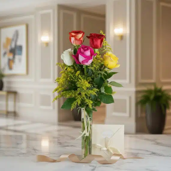 Solitario de rosas multicolor (roja, blanca, fucsia, amarilla, naranja) en jarrón de cristal con follaje verde, sobre mármol